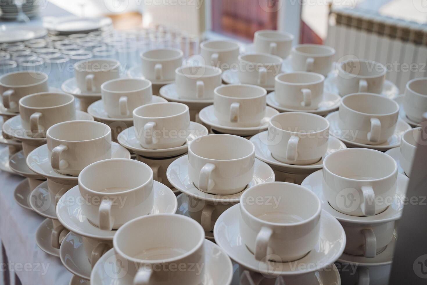 An elegant table is adorned with an abundance of pristine white coffee cups accompanied by matching saucers, creating a delightful setting for enjoying beverages and hospitality photo