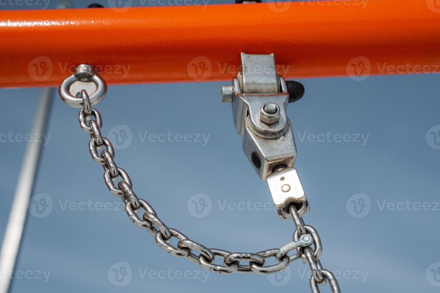 A closeup view showcasing a metal pulley accompanied by a chain, which is mounted on a vibrant orange frame of playground equipment for outdoor fun and interactive activities photo
