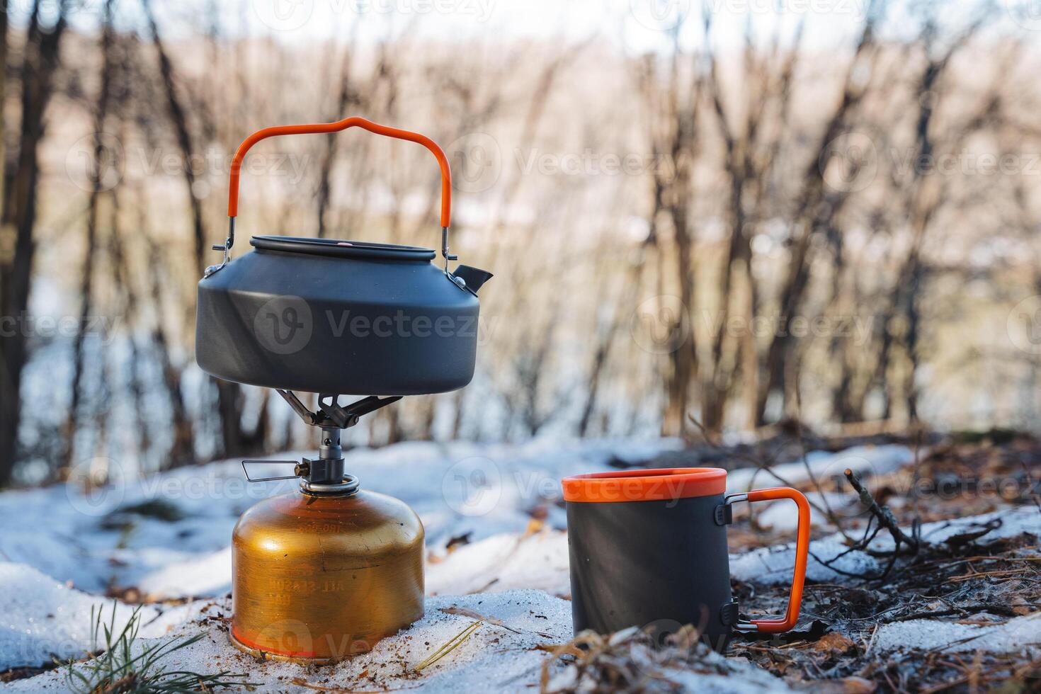 A kettle is placed on top of a gas cylinder, positioned right next to a cup, all resting in the cold snow, creating a unique kitchen scene amidst the wintery surroundings photo