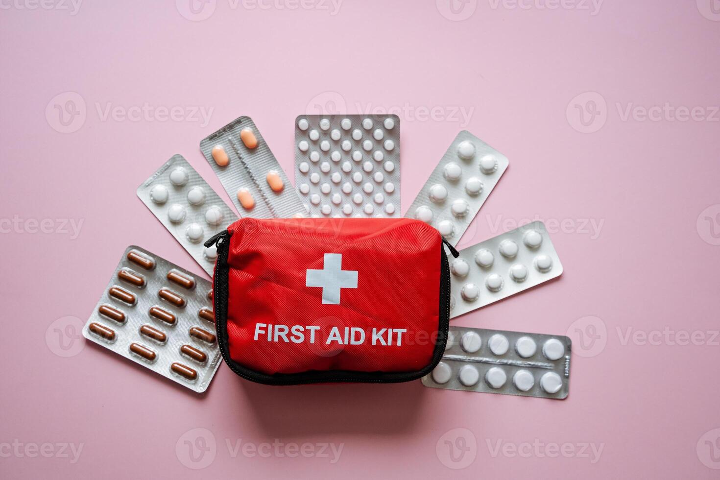 A WellStocked First Aid Kit is Carefully Positioned Amidst Various Medication Blisters Against a Soft Pink Background, Perfect for Healthcare and Recovery Needs photo