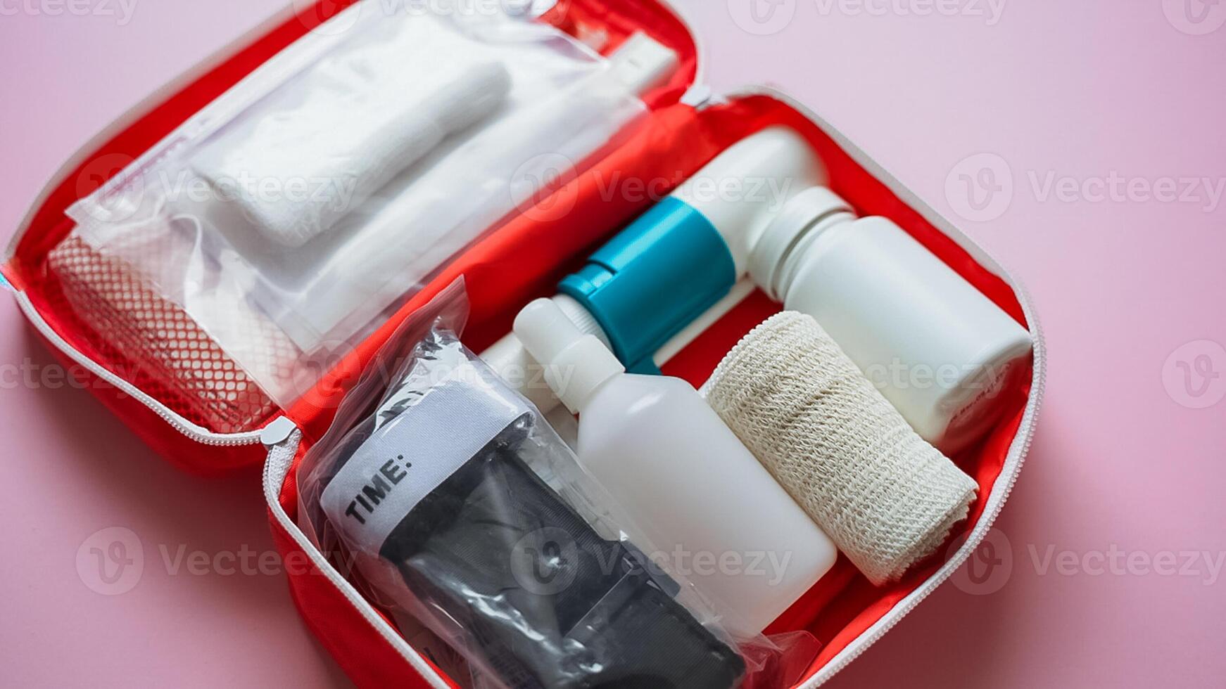 A bright red first aid kit that is filled to the brim with various bottles and an assortment of bandages, all set against a vibrant pink background that adds a cheerful touch photo