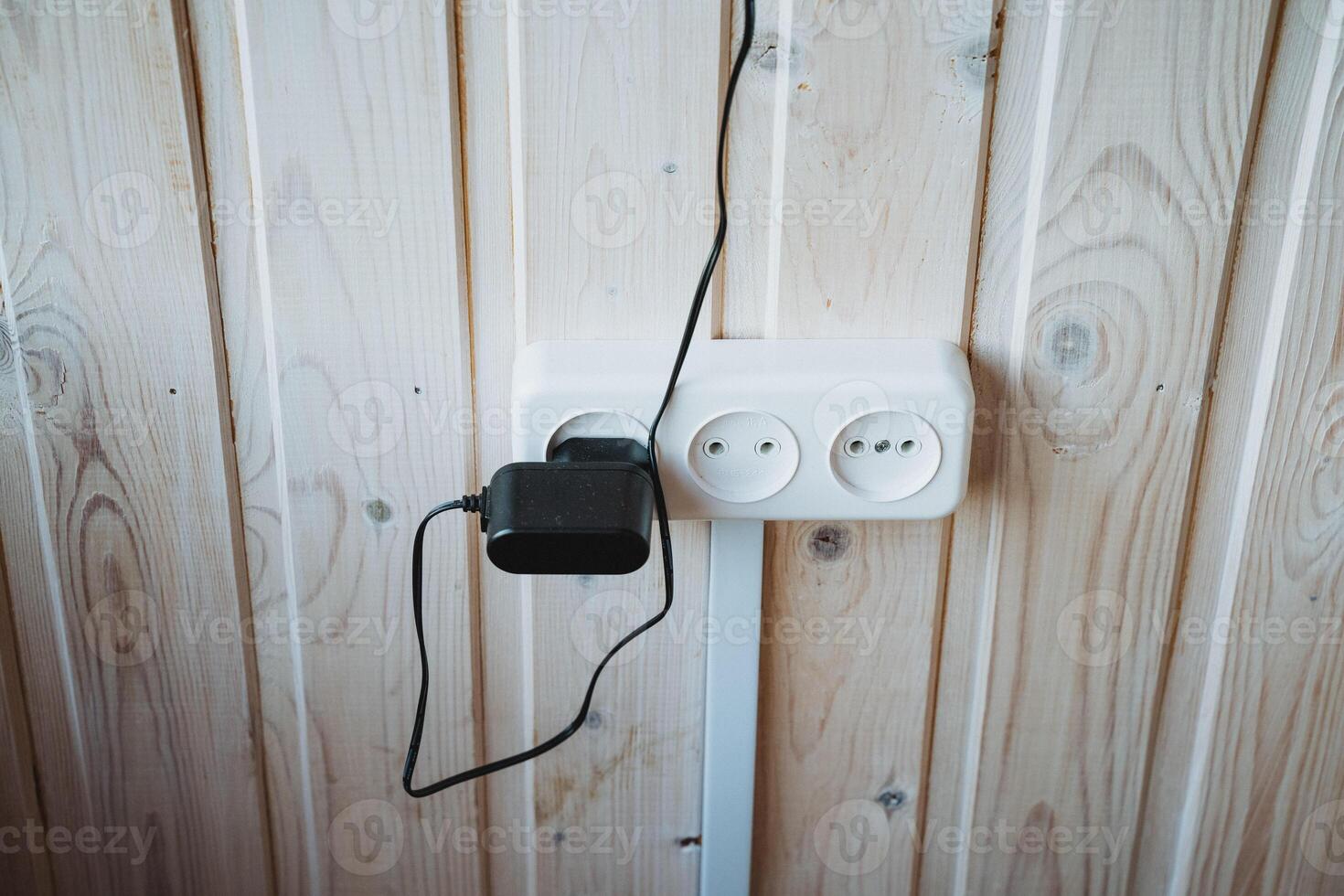 A charger is securely connected to a wall socket that is mounted on a strong, sturdy wooden wall, which allows it to effectively draw power for efficiently charging various devices photo