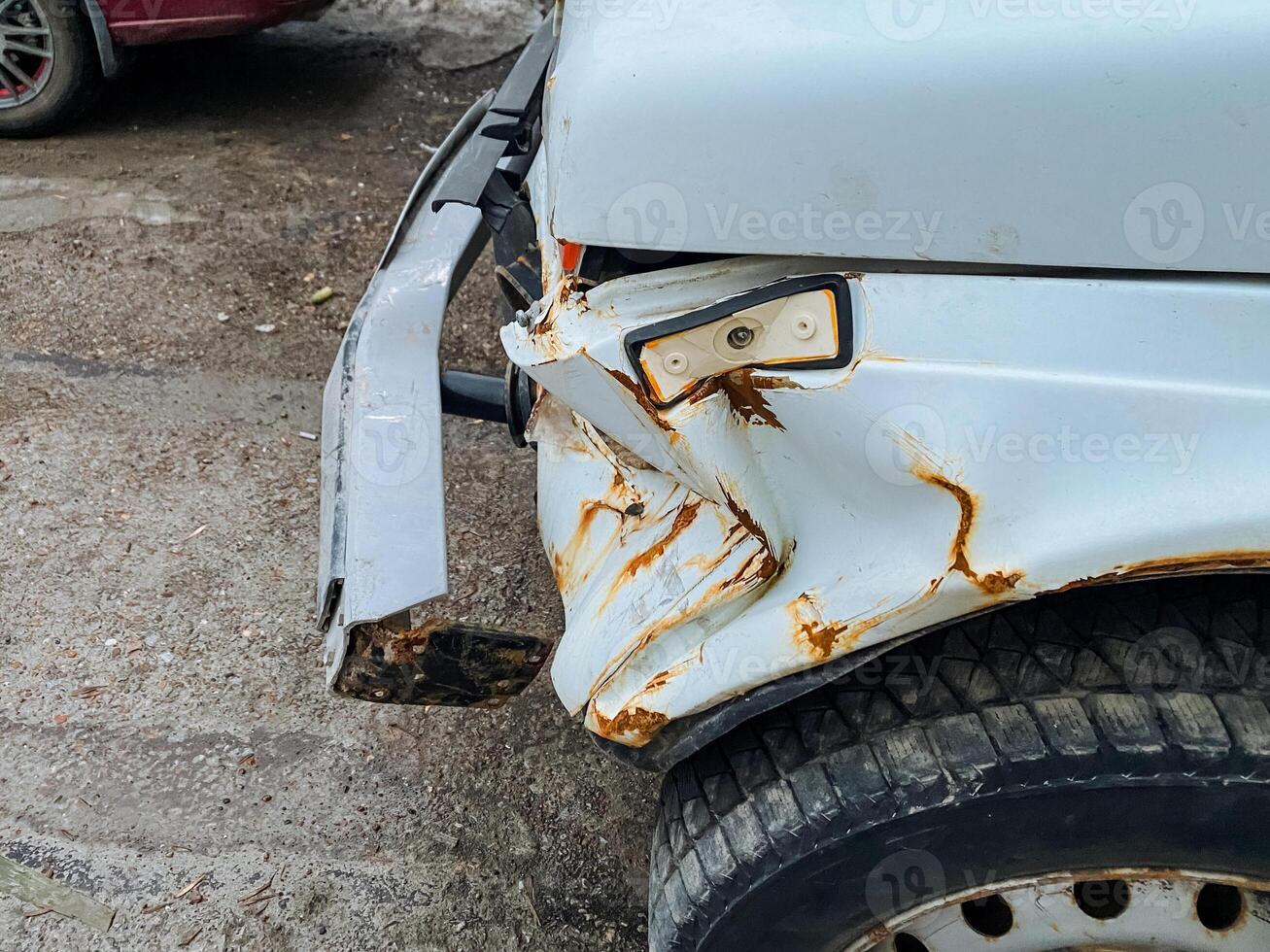 In a parking lot, there is a white car that has a visibly damaged bumper, indicating that it may have been involved in an accident or traffic collision, and is now parked there photo