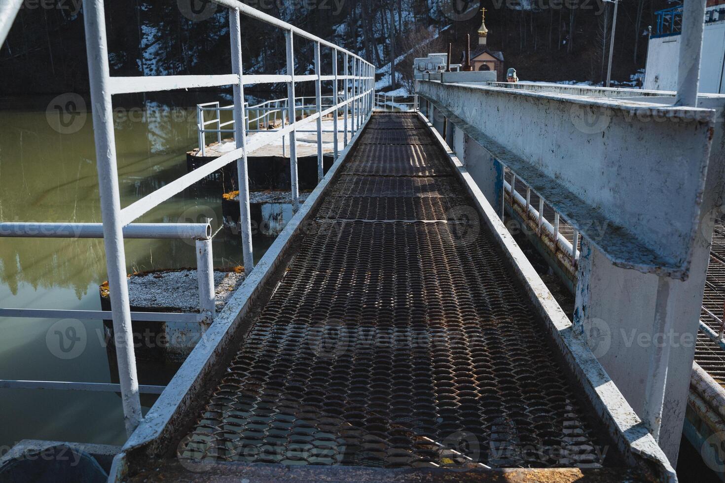 A sturdy metal bridge spans gracefully over a serene body of water, elegantly complemented by a white railing that enhances its beauty and safety for pedestrians crossing it photo