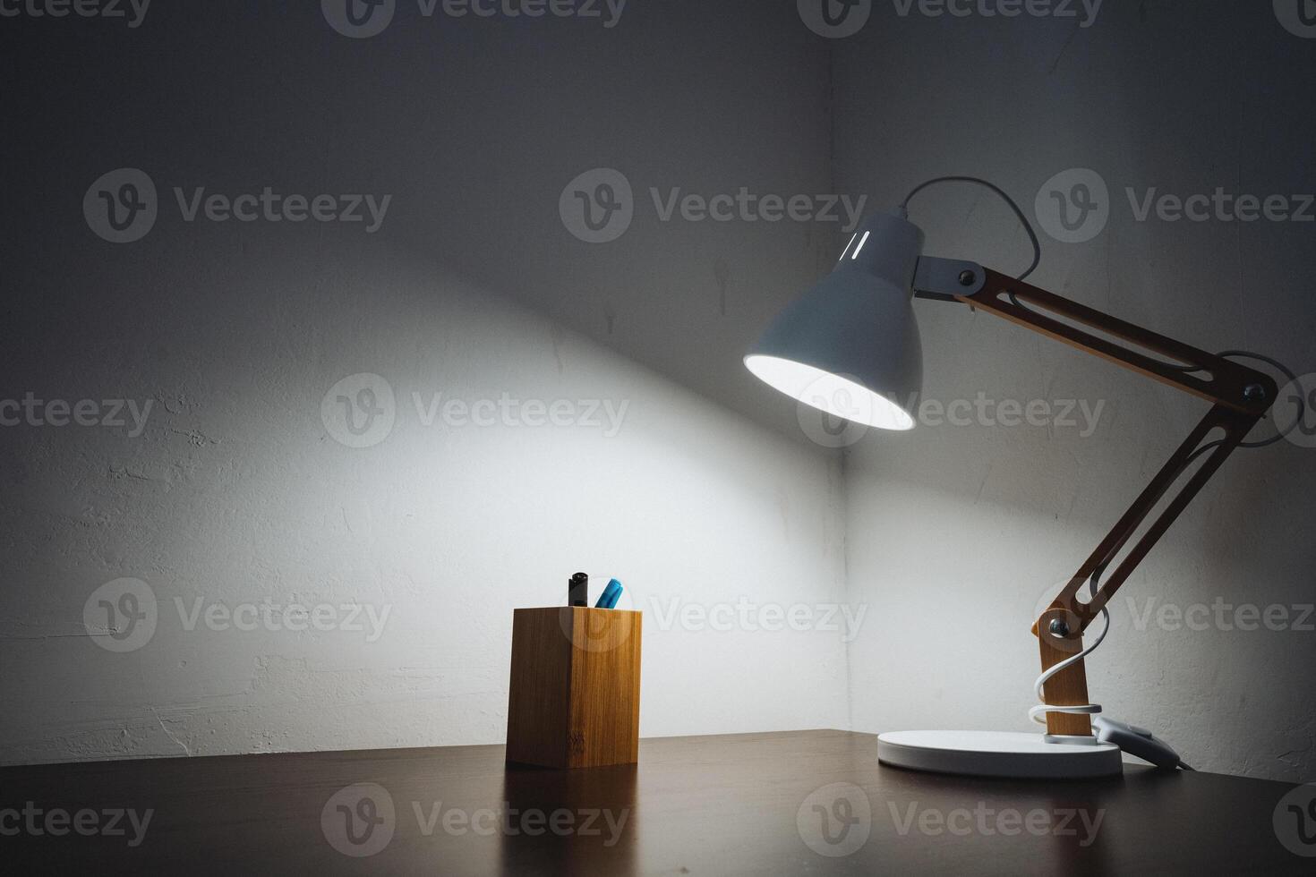A desk lamp is on a table next to a pen photo
