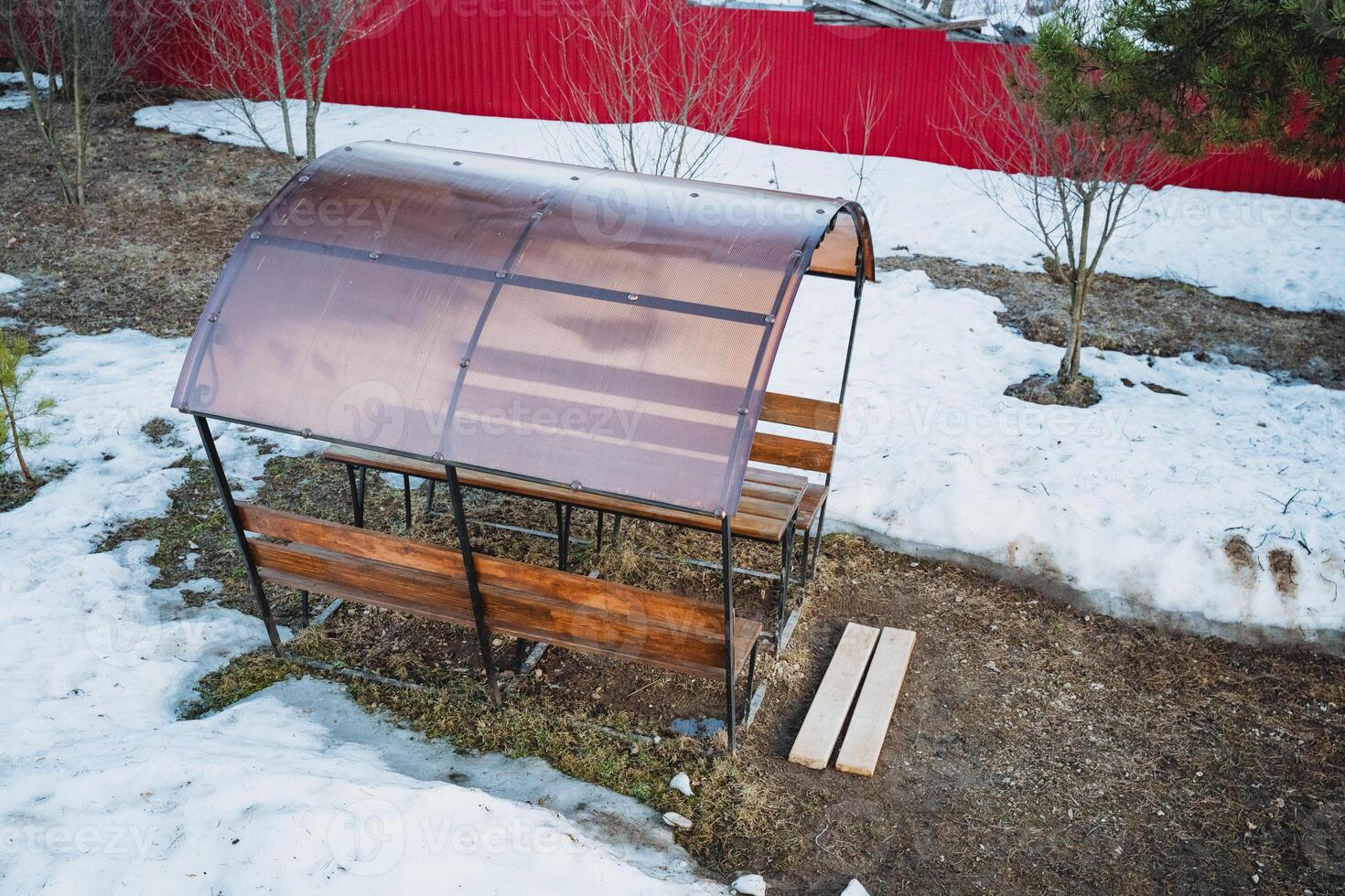 A sturdy wooden bench, complemented by a plastic roof, is currently resting in a thick layer of snow, showcasing an interesting juxtaposition of materials and natures beauty photo