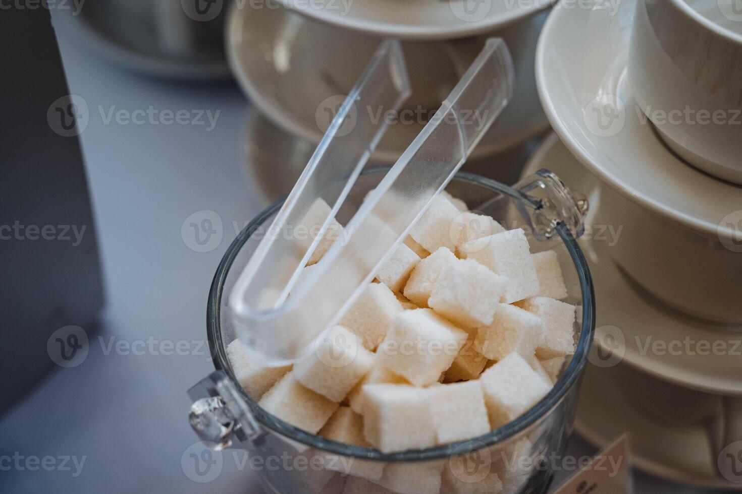 This elegant glass jar filled with sweet sugar cubes and tiny tongs adds practicality and charm to any kitchen or dining table, enhancing your culinary space and aesthetic appeal photo