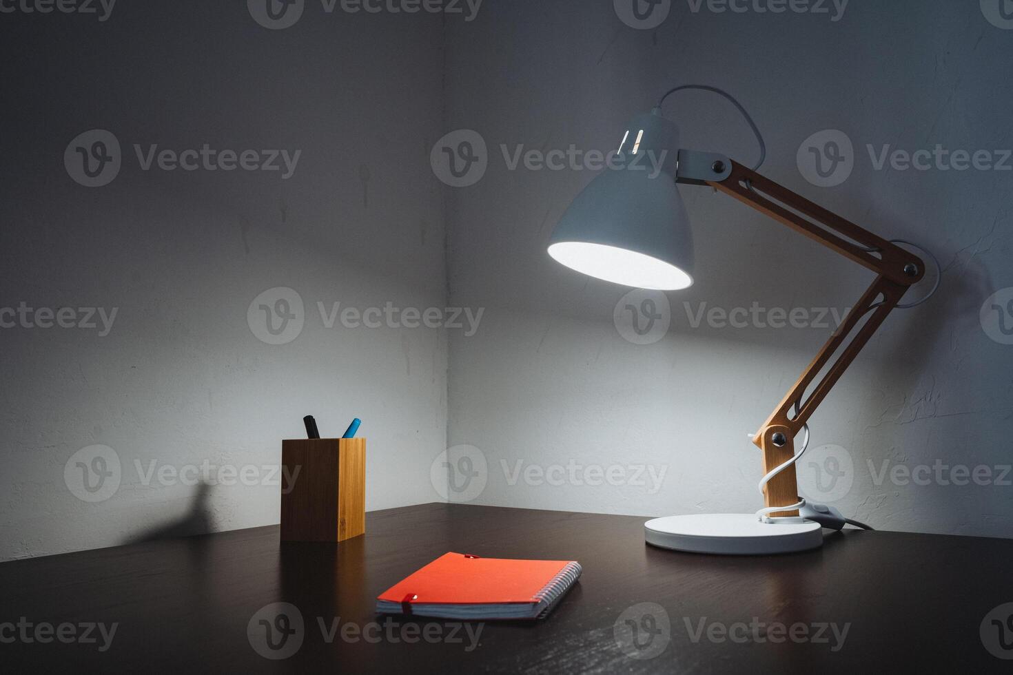 A stunningly crafted wooden desk paired with a stylish lamp illuminating an open notebook creates a warm and inviting workspace that truly fosters and encourages a flow of creativity photo