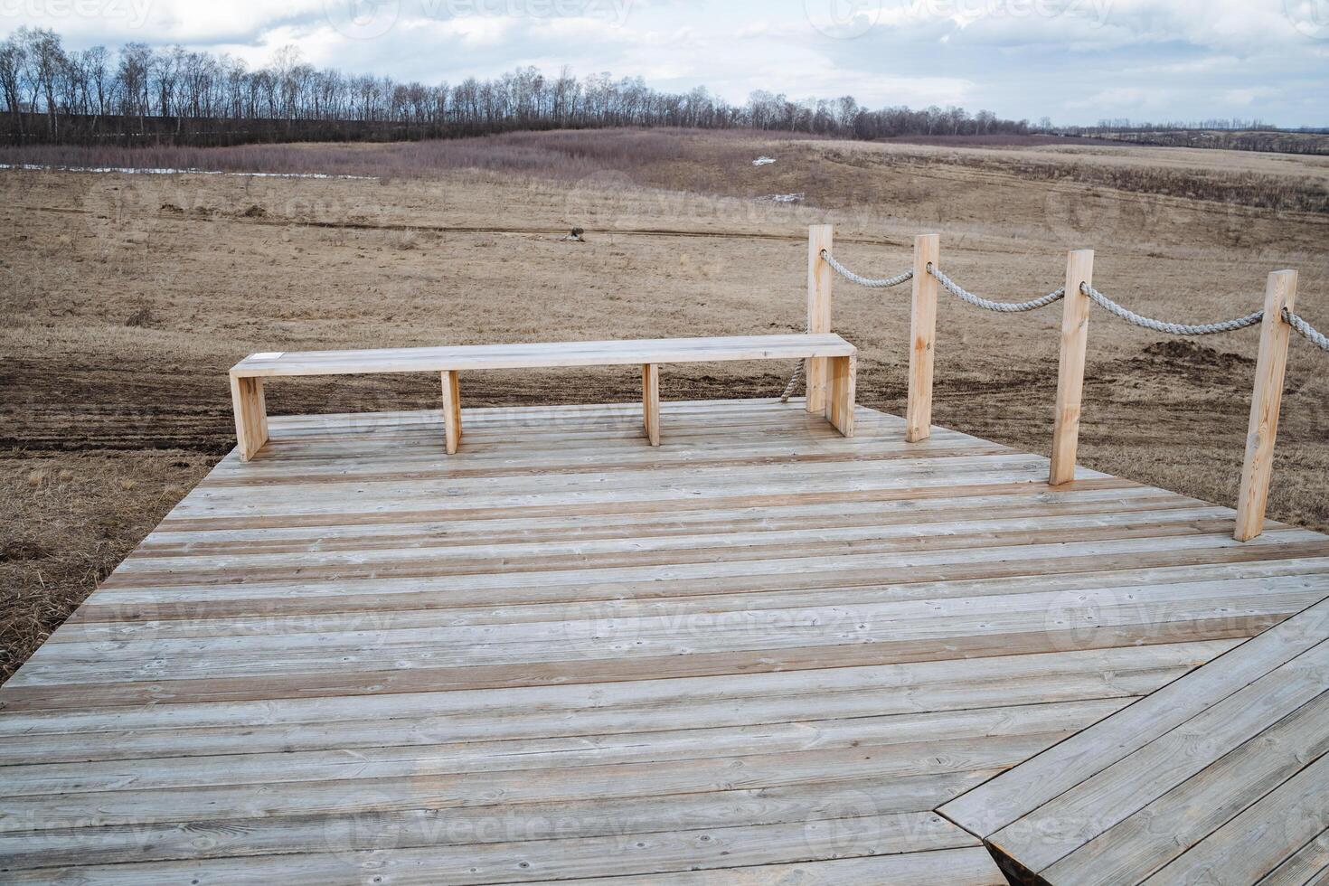 A scenic wooden deck featuring a comfortable bench positioned on it, allowing for relaxation, with a vast, open field visible in the backdrop, creating a beautiful outdoor atmosphere photo