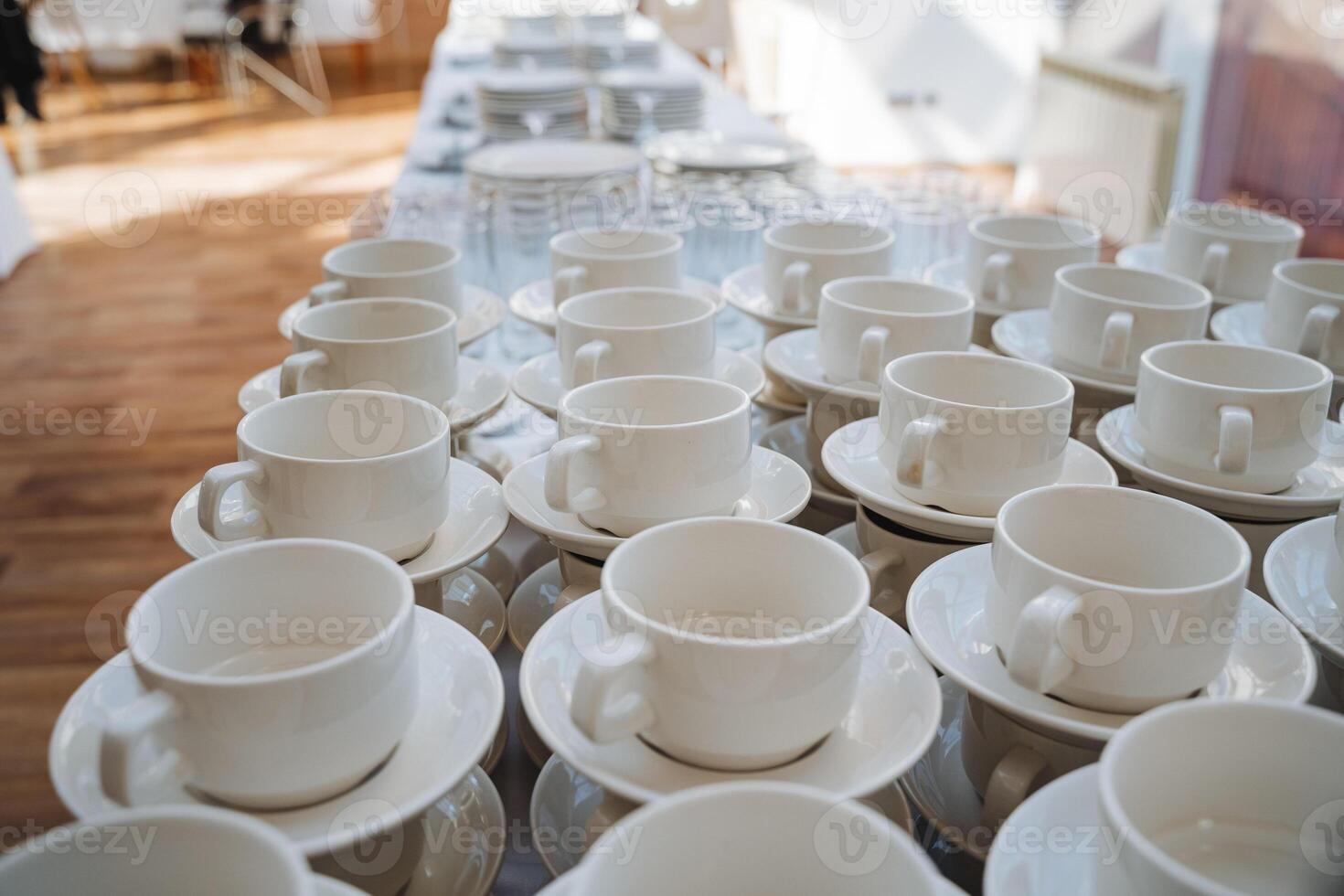 On a beautifully arranged table, there is a row of pristine white coffee cups delicately placed alongside matching saucers, creating an elegant display of serveware and tableware photo