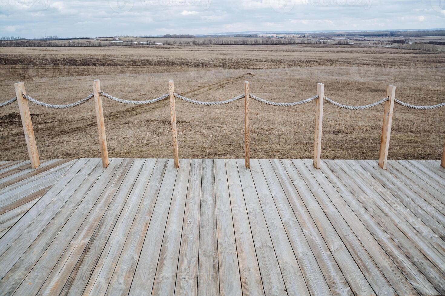 A beautiful wooden deck complete with a sturdy rope fence that offers a stunning view of a vast, open field stretching out before you, creating a sense of serenity and connection to nature photo