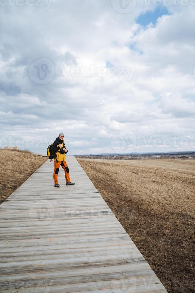 A solitary individual stands peacefully atop a wooden walkway that gracefully extends over an expansive field, taking in the breathtaking scenery and refreshing air in this serene setting photo