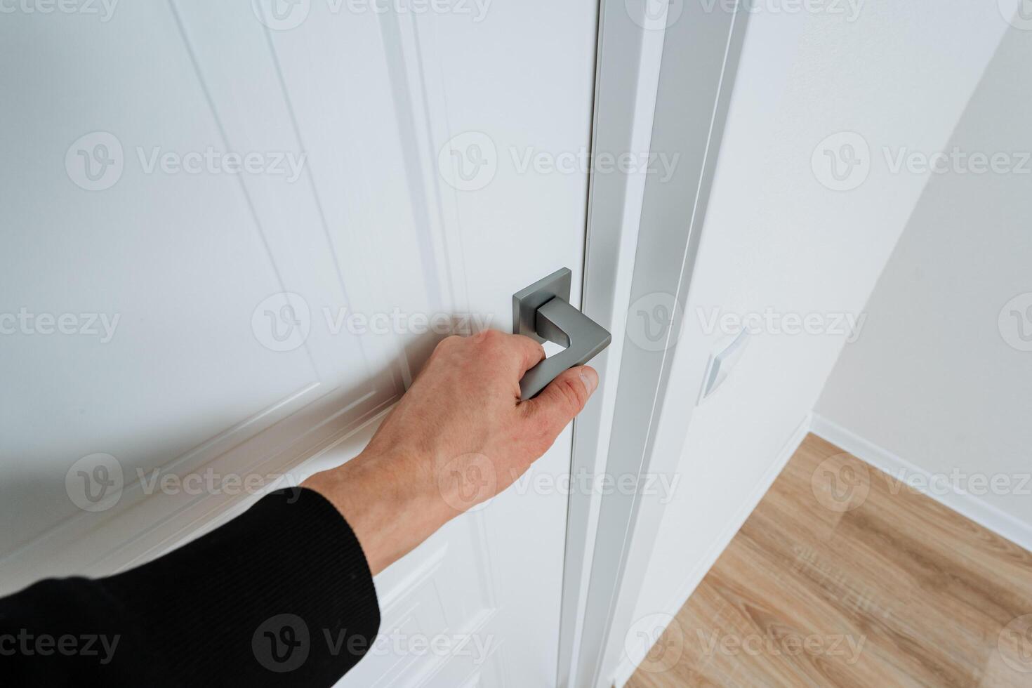 An individual is carefully opening a pristine white door with a shiny silver handle, revealing a cozy living space, sparking curiosity about the fascinating things inside photo