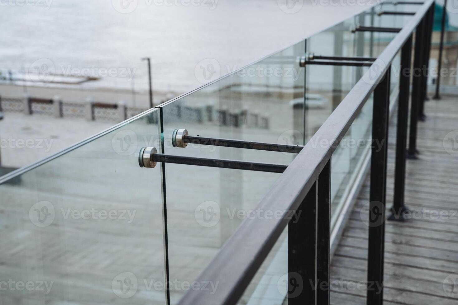 The photograph features a close up view of a sleek glass railing situated on a balcony that offers a stunning perspective overlooking the vast and beautiful ocean beyond photo