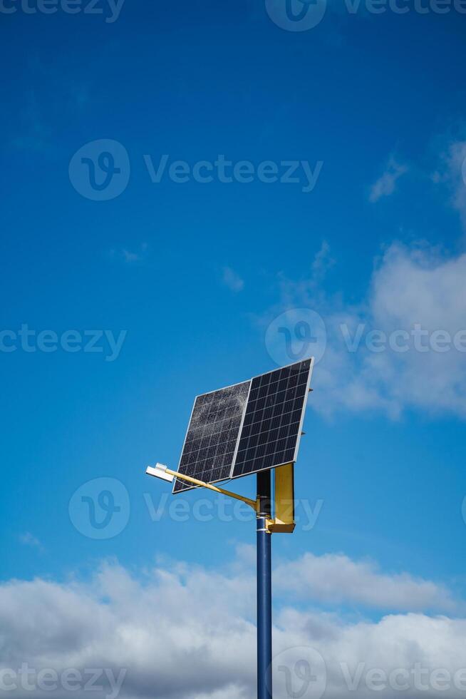 In the foreground, there is a solar panel securely mounted on a tall pole, and in the background, the sky shines bright and blue, creating a picturesque scene of renewable energy photo