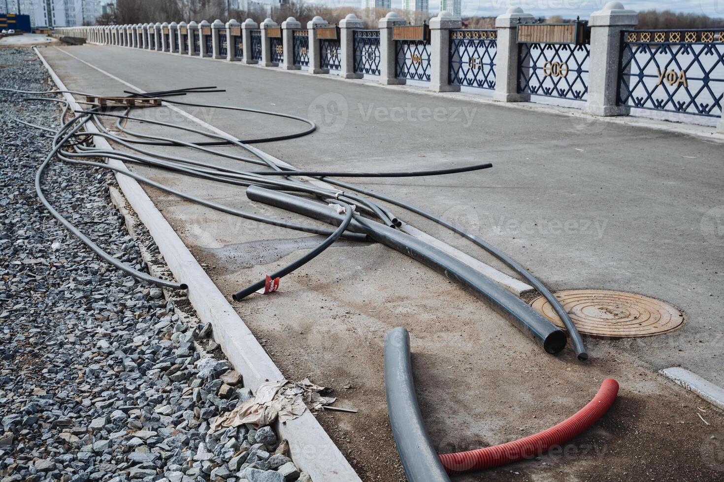 A messy and tangled mass of various wires is carelessly spread out on the ground near a bridge, which poses a significant hazard to pedestrians and passersby who may be in the area photo