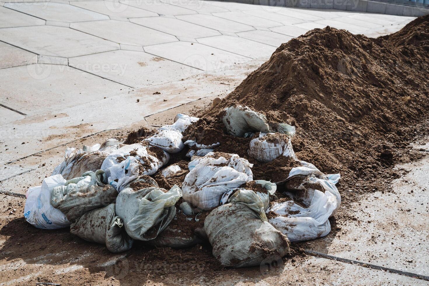 A large pile of dirt is resting on the ground, situated right next to an adjacent pile that consists of bags filled with dirt, both of which are contributing to local pollution issues photo
