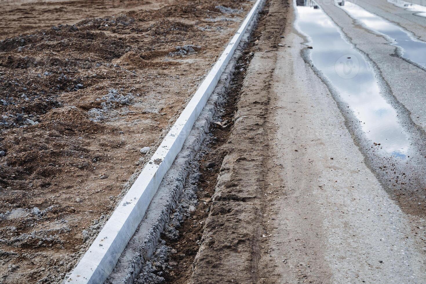 A highly durable concrete curb is currently being installed along a road in order to clearly define the designated space and significantly enhance the overall visual appearance of the area photo