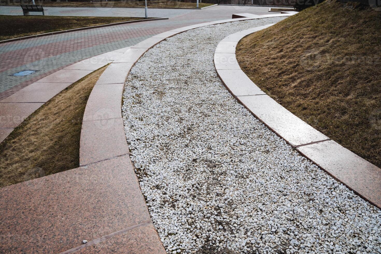 A beautifully designed curved walkway features gravel elegantly lining its side, enhancing the aesthetic and functionality of the public space while providing a pleasant walking experience photo
