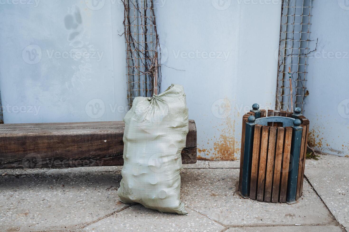 A bag filled with garbage is currently sitting right next to a wooden trash can, which provides an interesting contrast in this still life composition that captures everyday objects photo