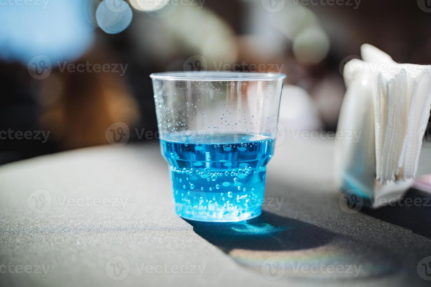 A plastic cup, brimming with a vibrant blue liquid, is placed on a table, catching the eye with its striking color and simple elegance, perfect for serving cold beverages photo