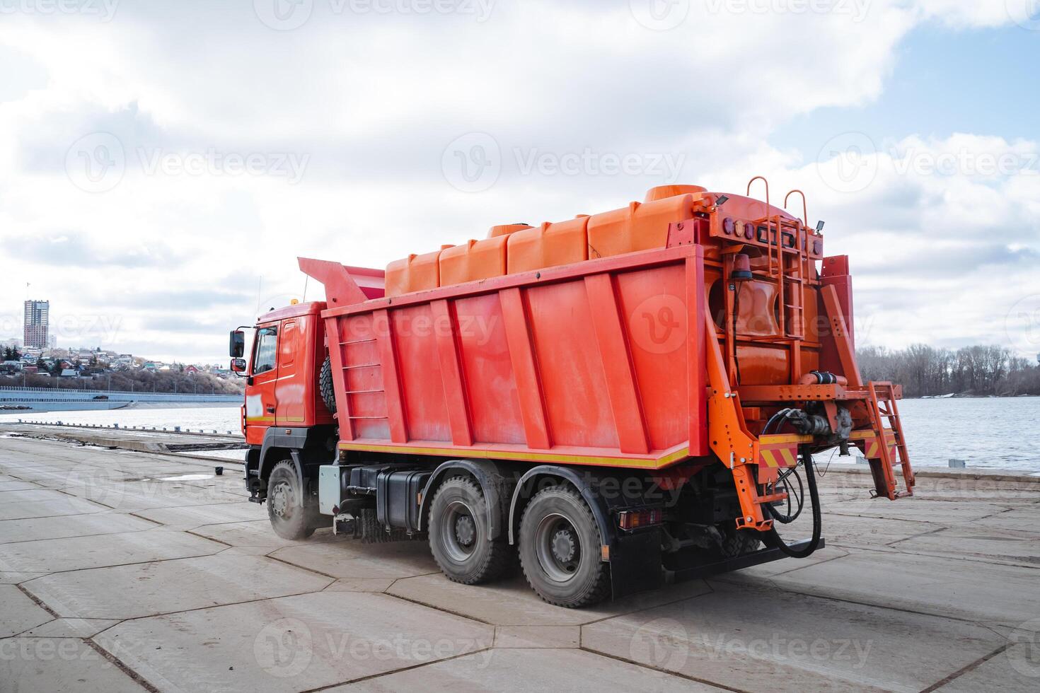In a spacious parking lot, a bright red dump truck is parked next to a stunningly large and beautiful body of water, creating a picturesque scene that everyone can admire and appreciate photo