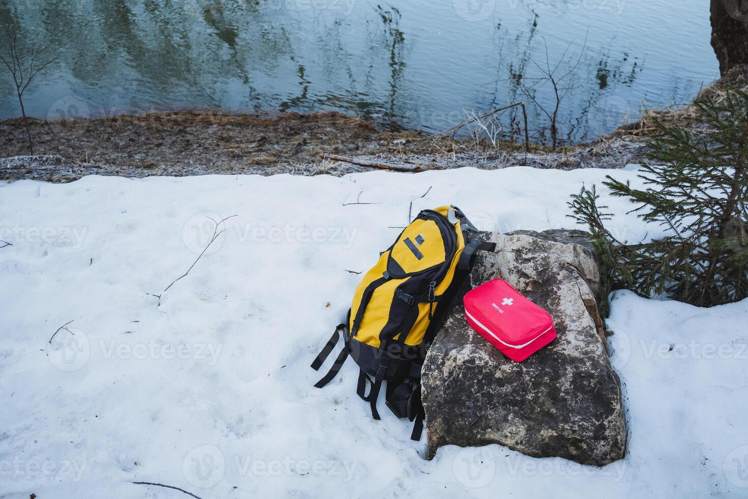 In the midst of an untouched snowy landscape, a bright yellow backpack lies on a weathered rock, creating a striking and vivid contrast against the pristine white snow of winter photo