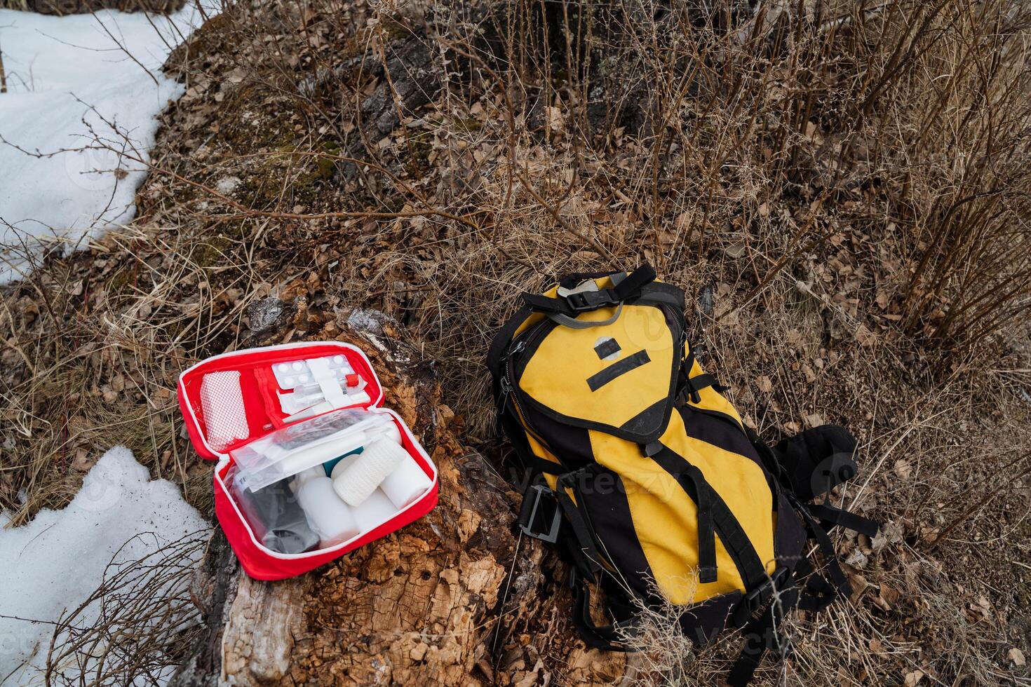 A vibrant yellow and black backpack is comfortably resting on the ground next to a bold, bright red first aid kit, creating a strikingly vivid contrast on the surface beneath them photo