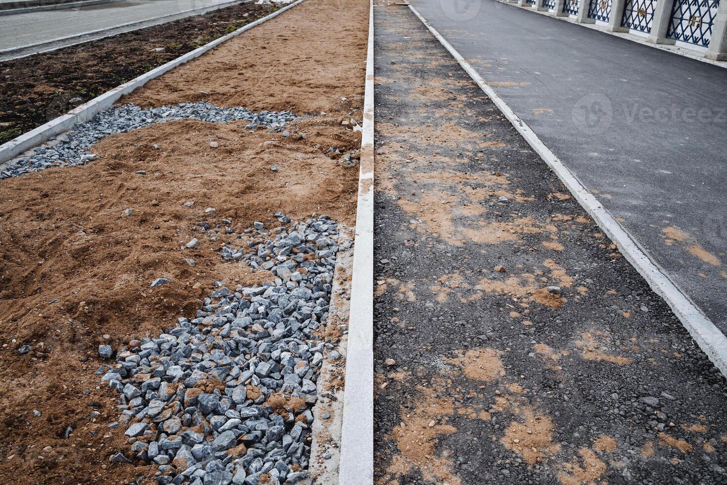 Next to a road that is currently under construction, there is a row of dirt and gravel, forming a rough terrain that will eventually support the finished roadway and sidewalks photo