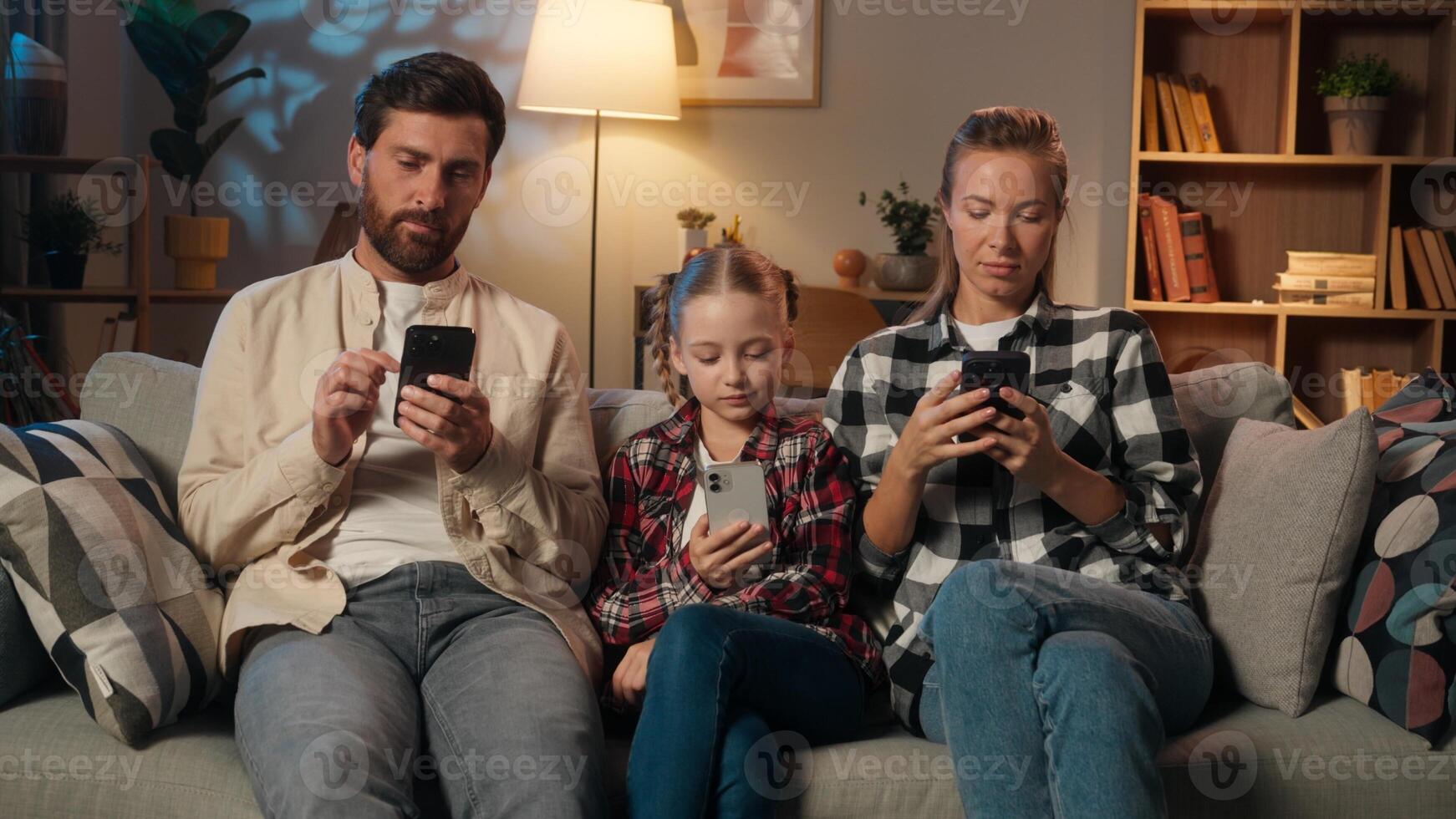 European family using mobile phones smartphones addiction dependency online internet gadgets at home in evening living room dad father yawning mother with child girl kid daughter relaxing together photo