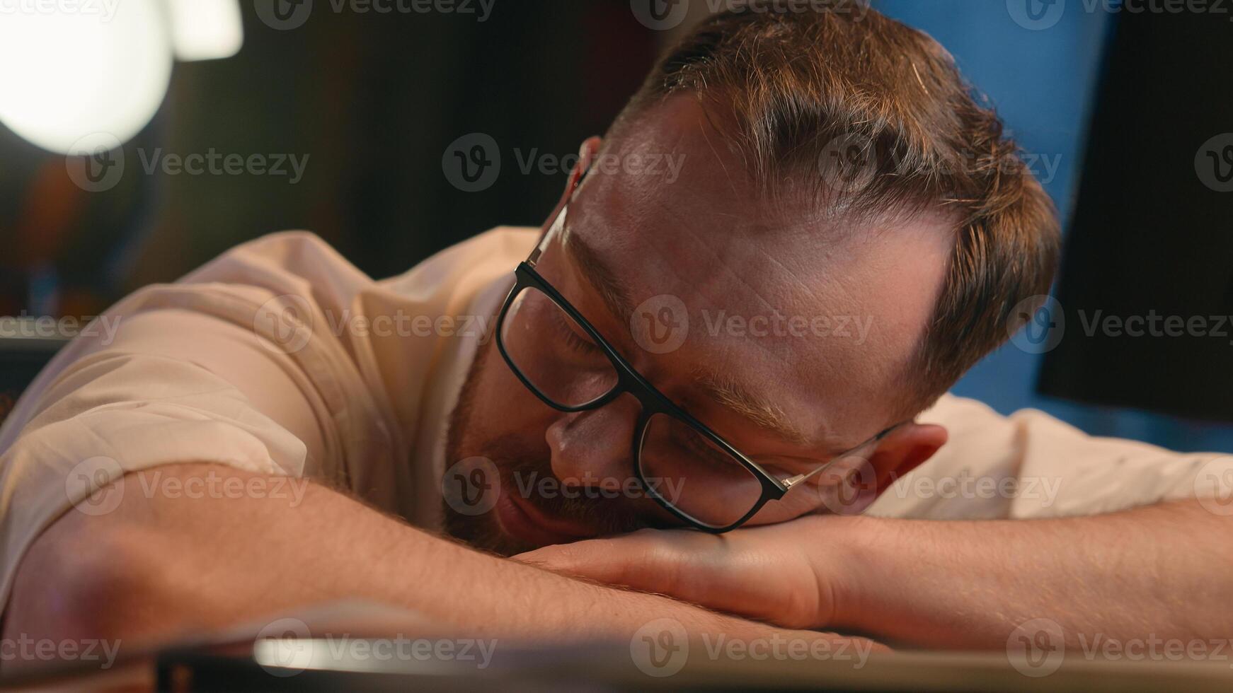 Caucasian man business guy businessman male workaholic in dark night office overworked overtime overload stress tired exhausted lying on table sleep napping late time sleep deadline health problem photo