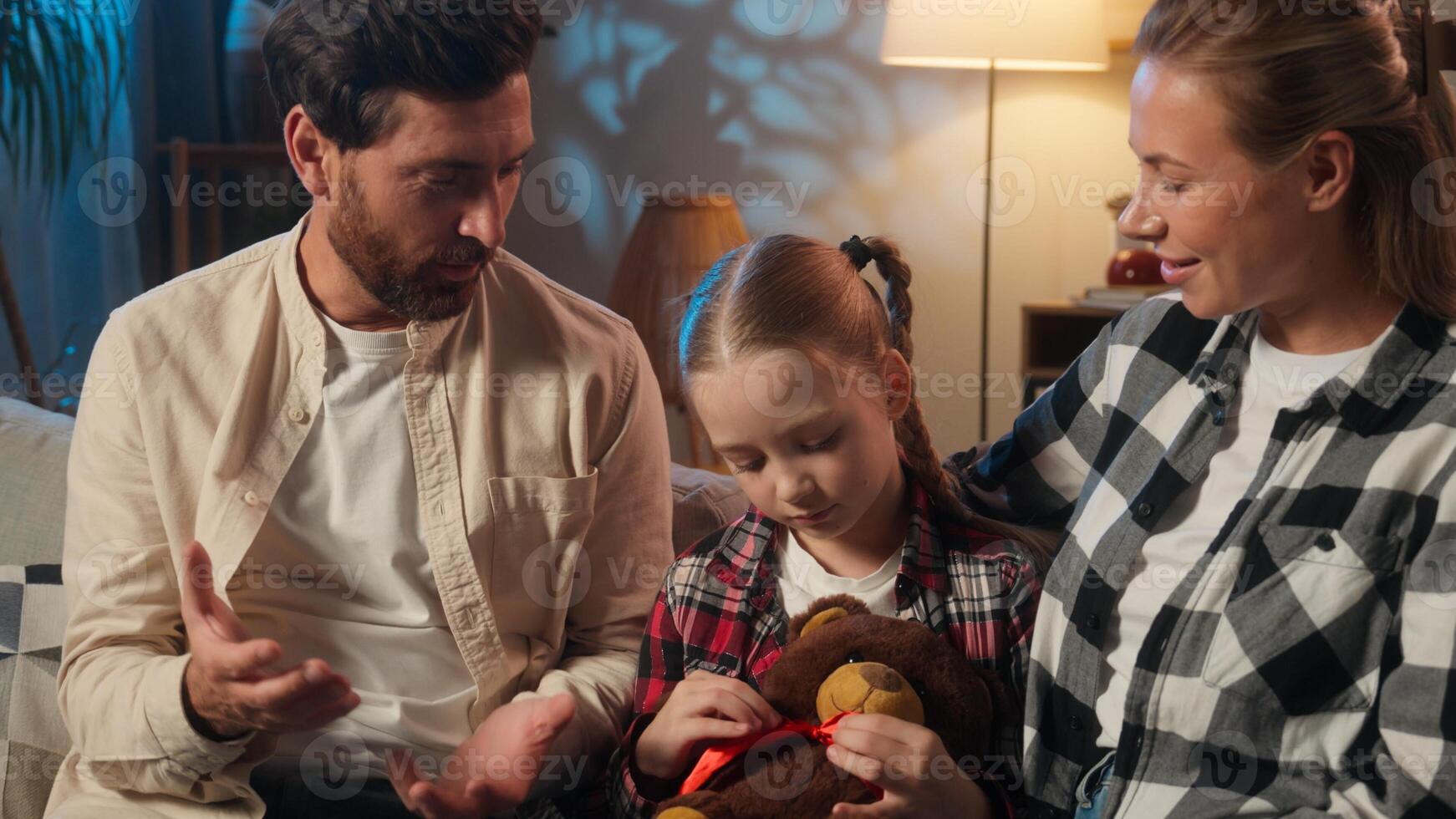 Happy European family at evening home talking parents hugging daughter talk conversation smiling relaxing on couch satisfied parents with child girl kid holding toy teddy bear adopt custody cozy rest photo