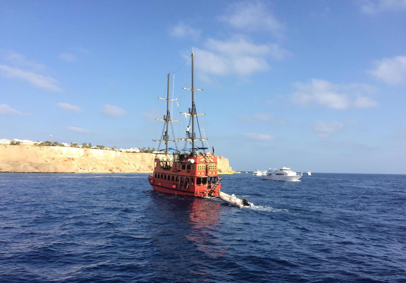 A bright pirate ship with a red hull and tall masts sails through the blue waters of the sea, leaving waves behind. photo