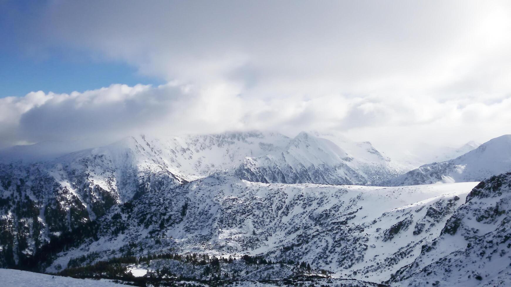 Clouds. Majestic winter landscape with snow-capped mountains, densely covered with coniferous forest. photo