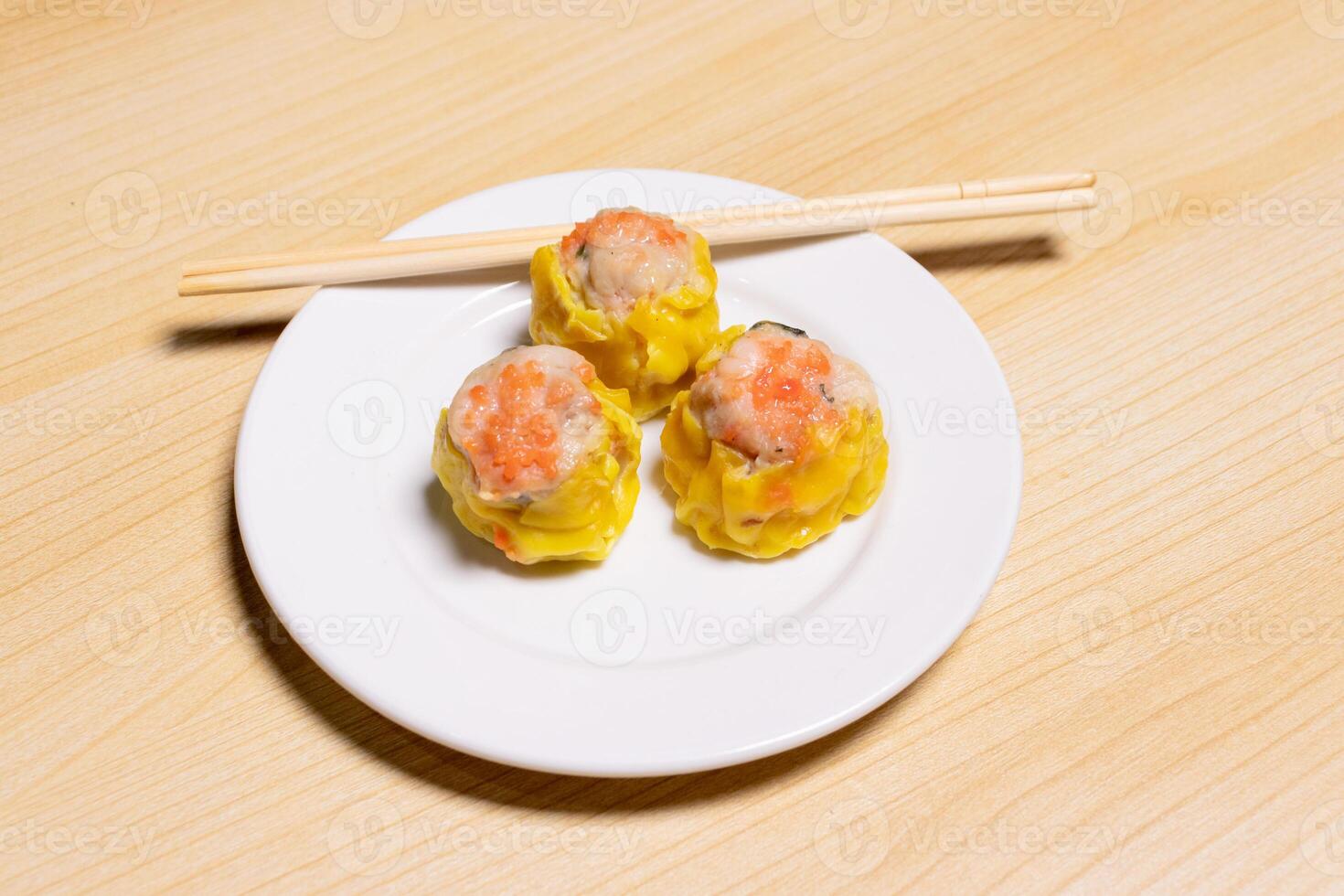 Dimsum and chopsticks on white plate isolated on wooden background. After edits. photo