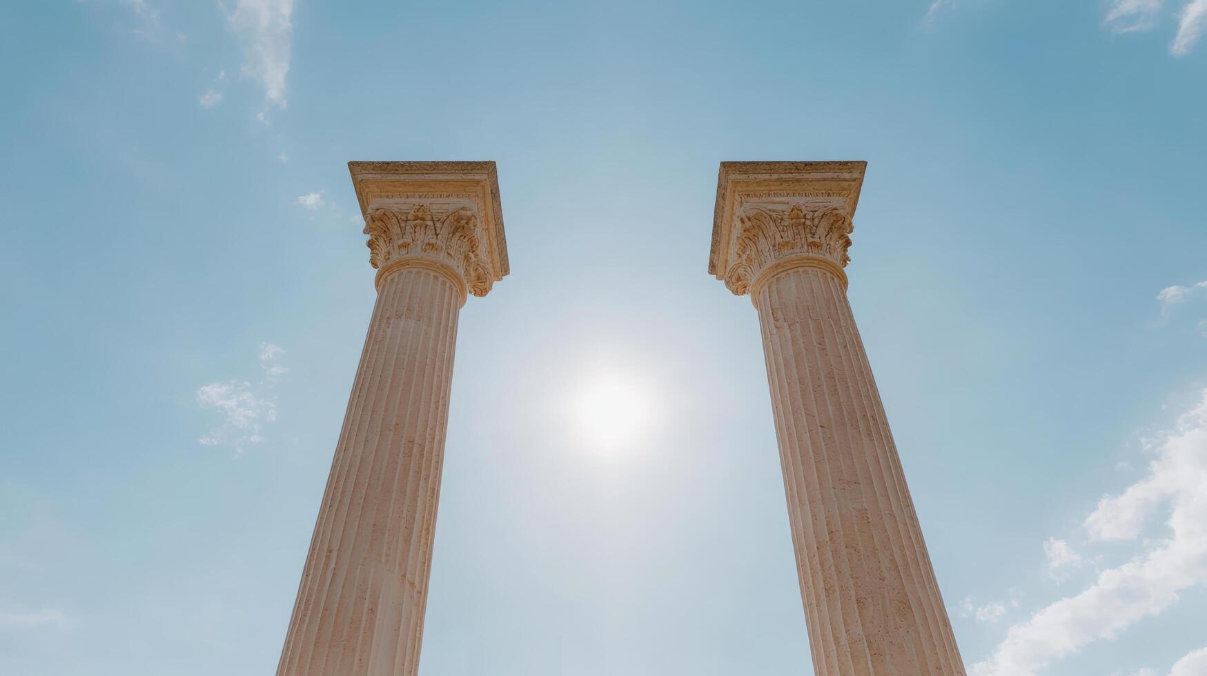 Tall stone columns reach towards bright sun in clear blue sky, evoking sense of grandeur photo