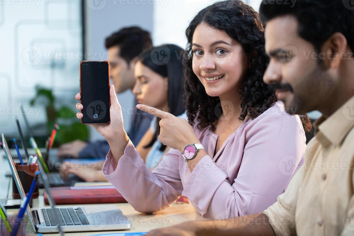 Female Employee Female Sitting On Office Desk Pointing On Mobile Phone Screen photo