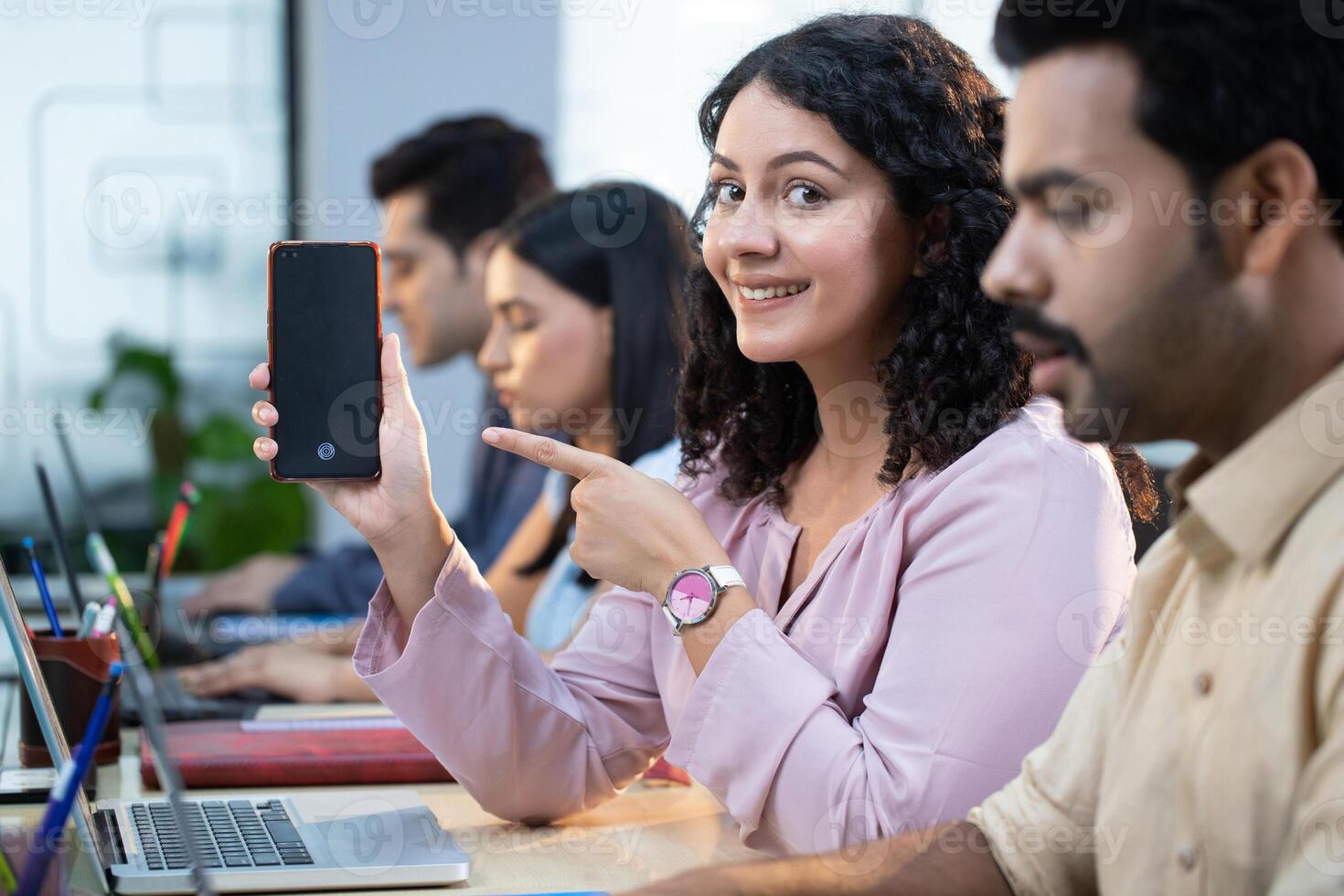 Office Employee Female Sitting On Office Desk Pointing On Cell Phone Screen photo