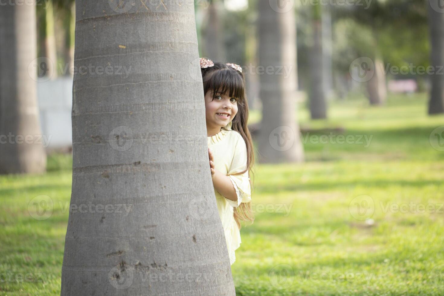 Cute Little Girl Peeking From Behind A Tree photo