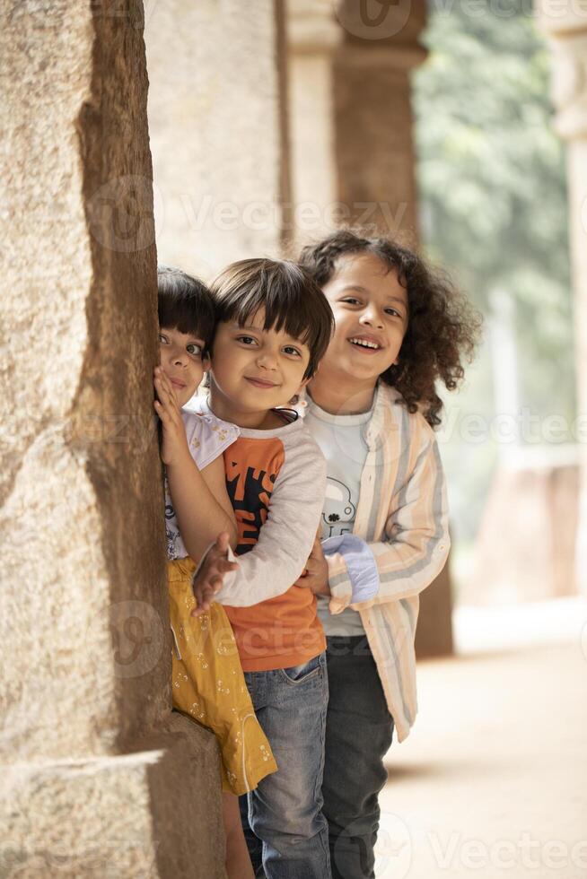 Little Children Posing In Front Of Camera While Standing Behind Ancient Column photo