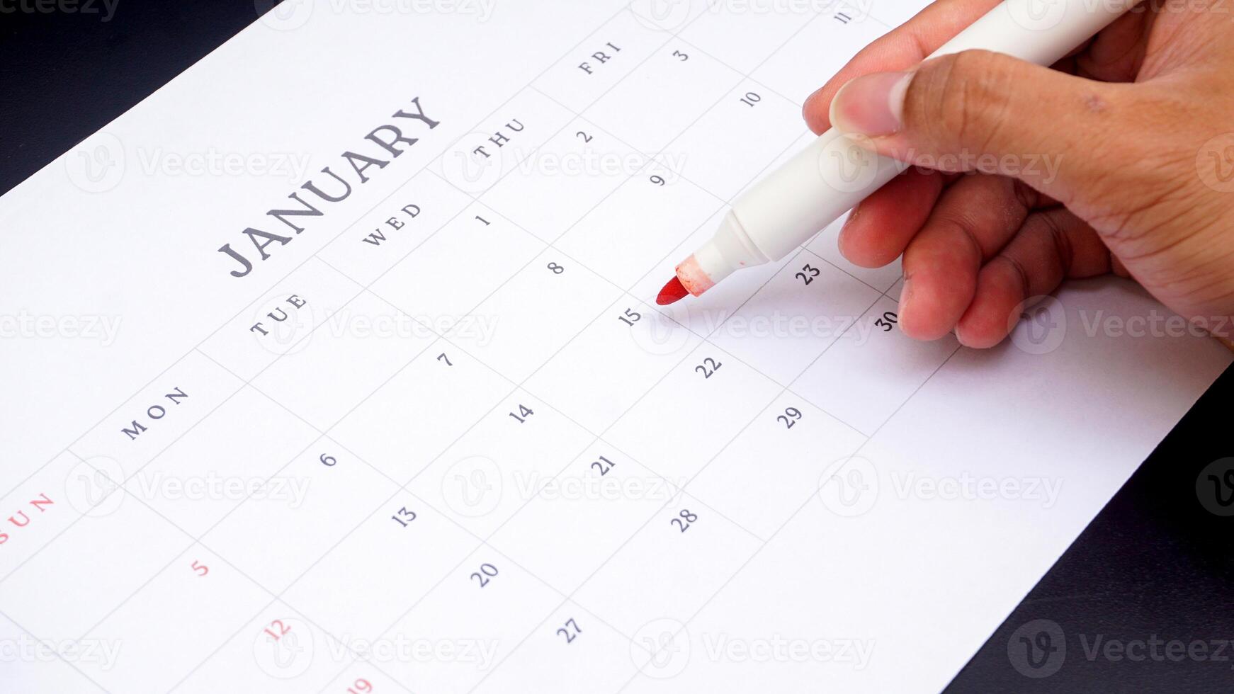 Hand holding marker to make mark on calendar isolated on black background photo