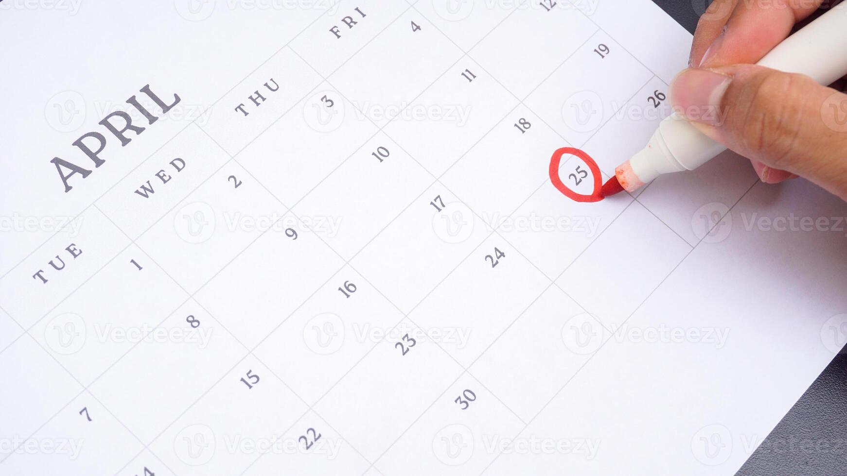Red circle marked on a calendar at 25 of April isolated on black background for an important day photo