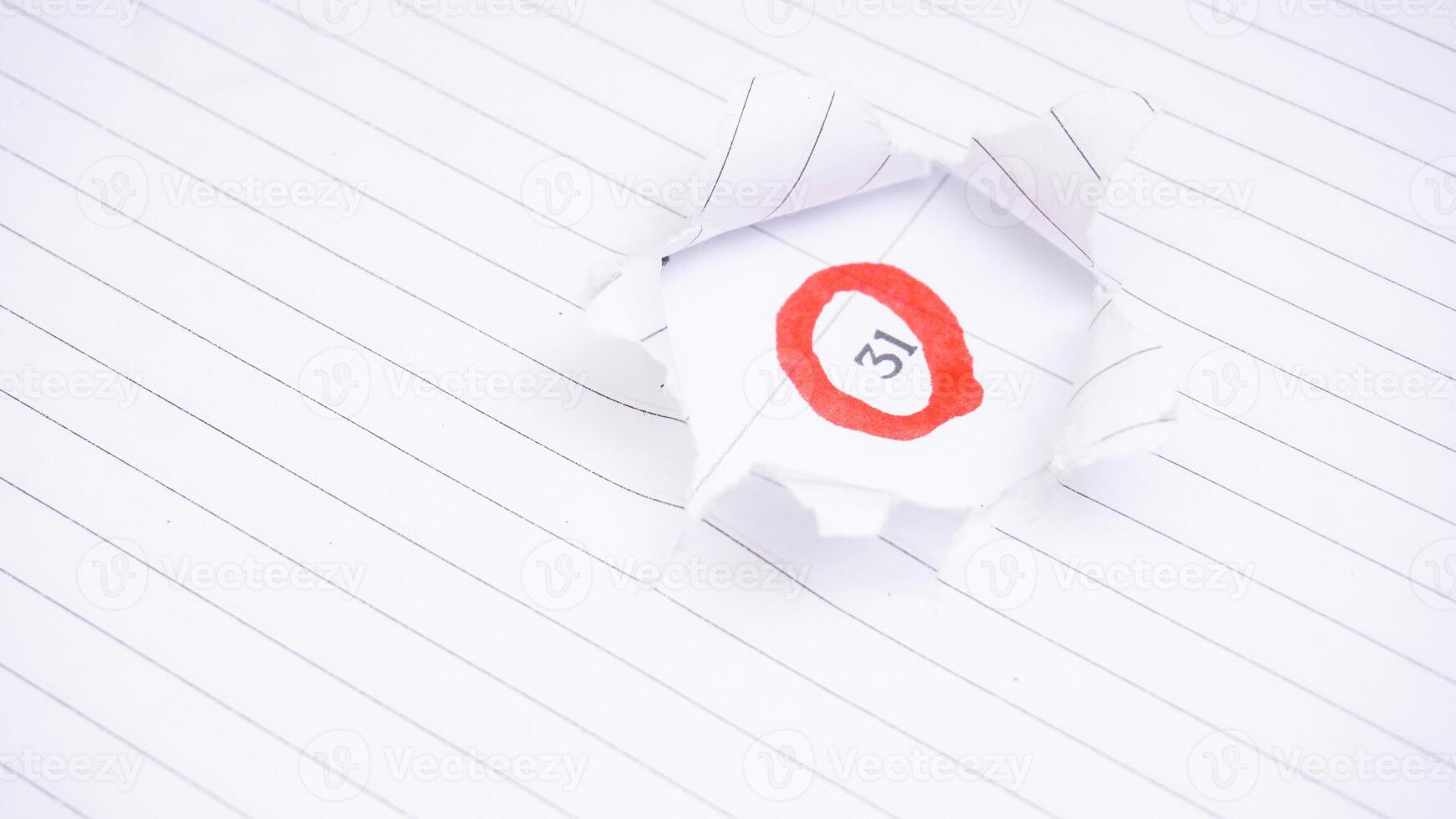 Ripped hole in white paper showing red circle marked on calendar at 31 photo