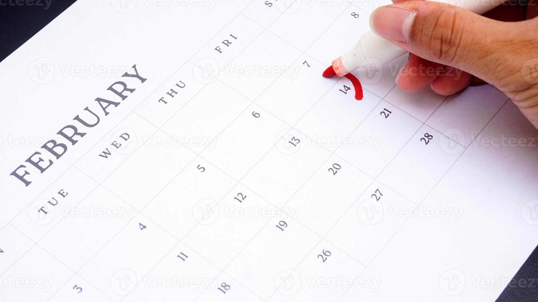 Hand holding marker to make mark on calendar at 14 of February as symbol of valentine day isolated on black background photo