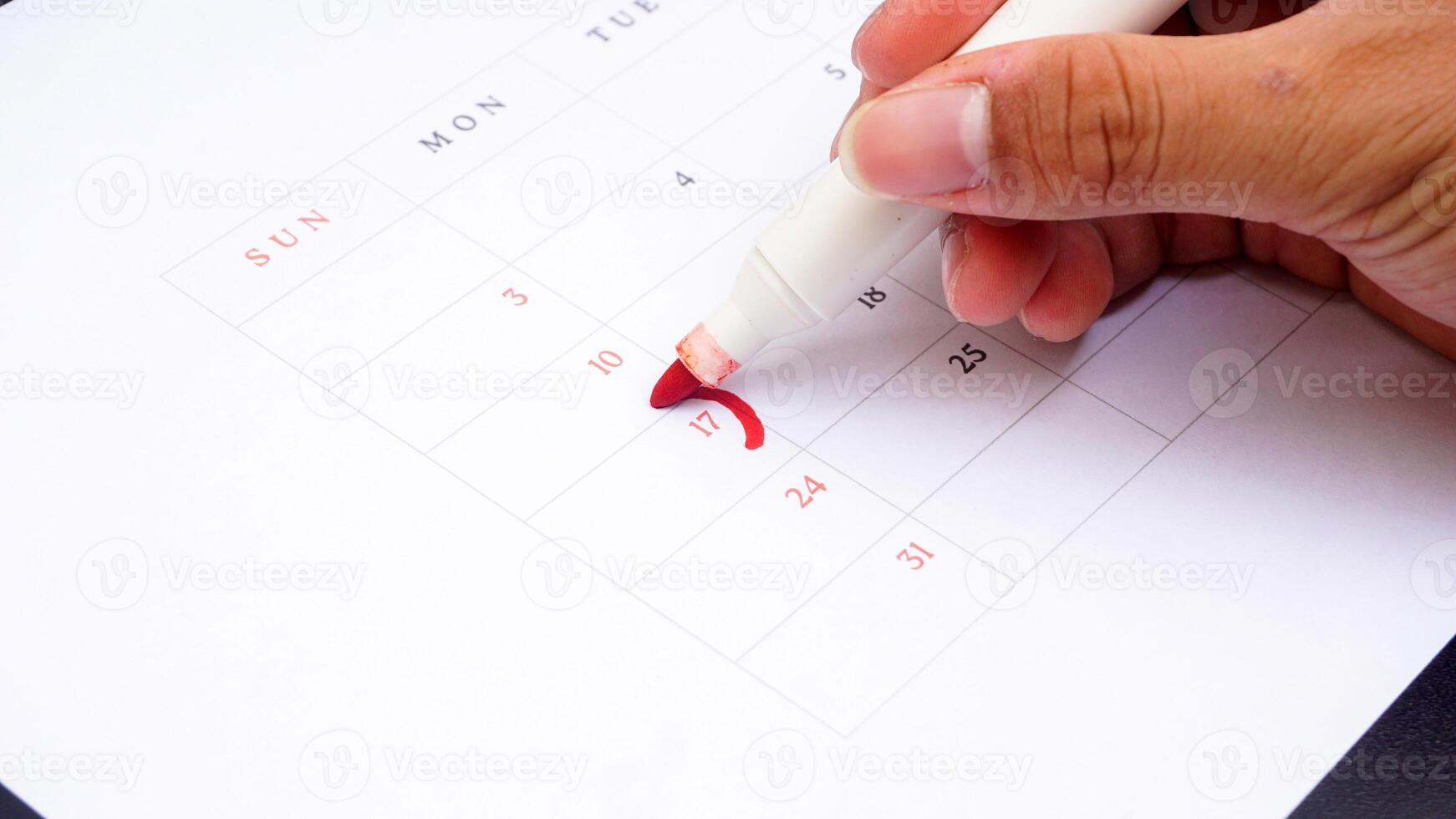 Hand holding marker to make mark on calendar at 17 isolated on black background photo