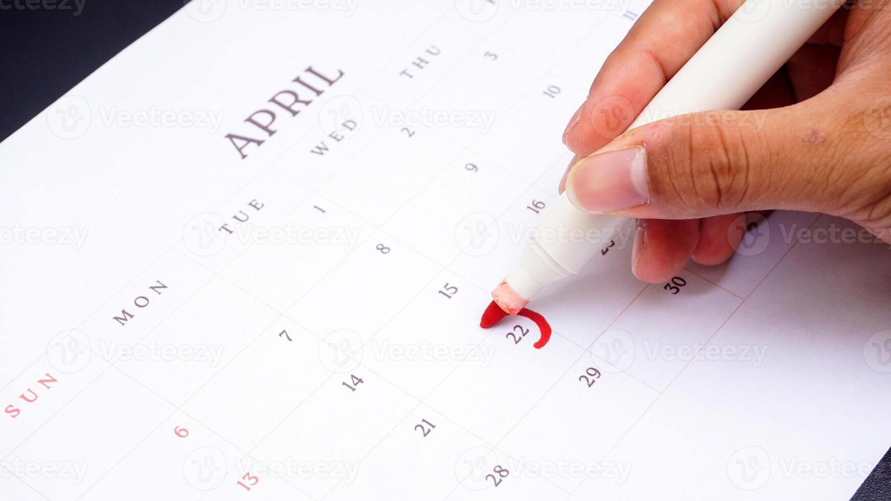 Hand holding marker to make mark on calendar at 22 of April as symbol of important day isolated on black background photo