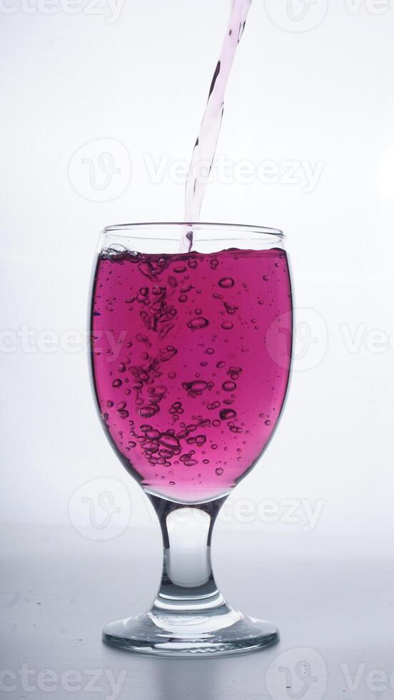 Purple colored water poured into transparent glass isolated on white background photo