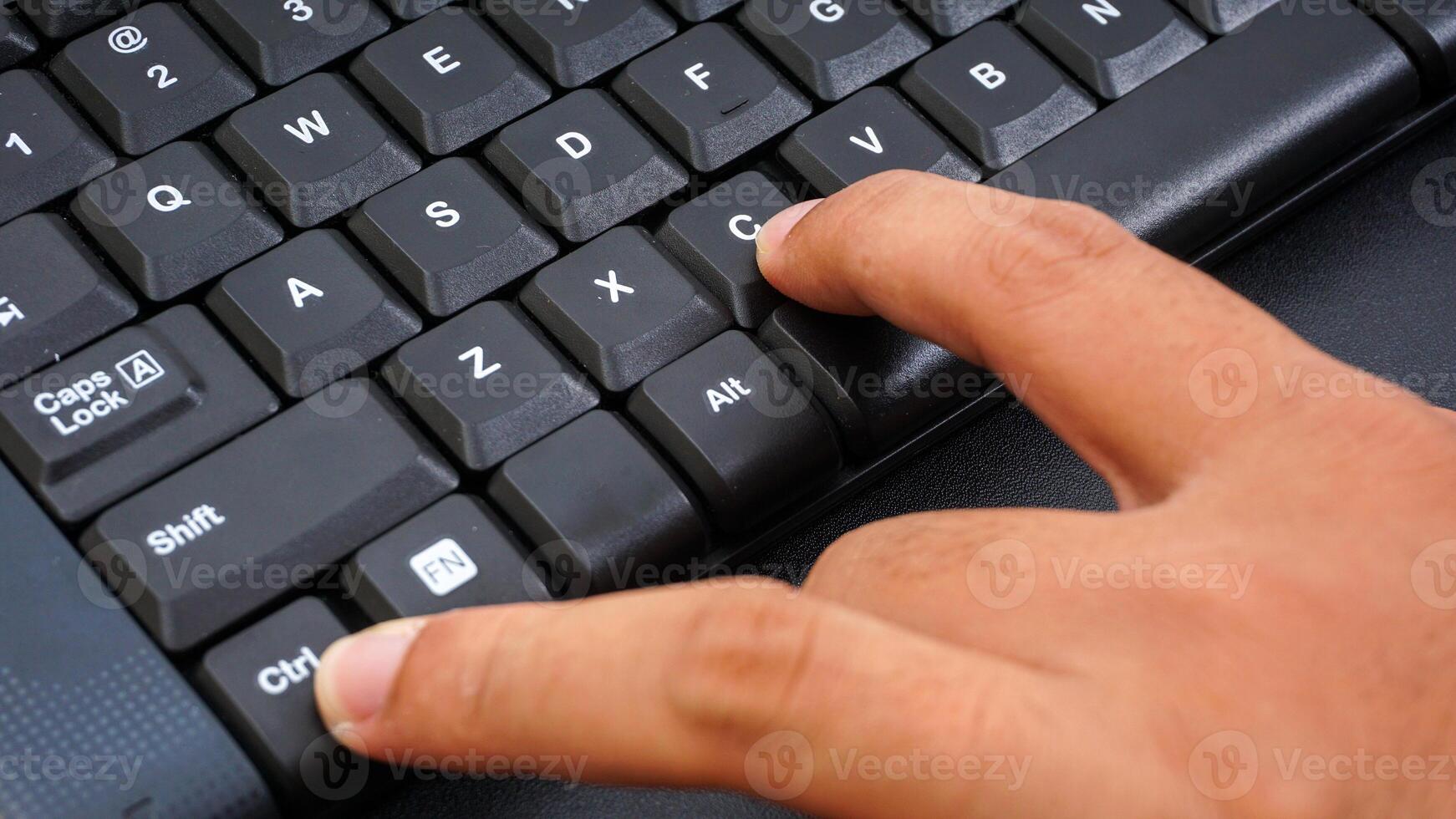 Close up on finger pressing ctrl or control and c shortcut keys on a computer keyboard for copy isolated on black background photo