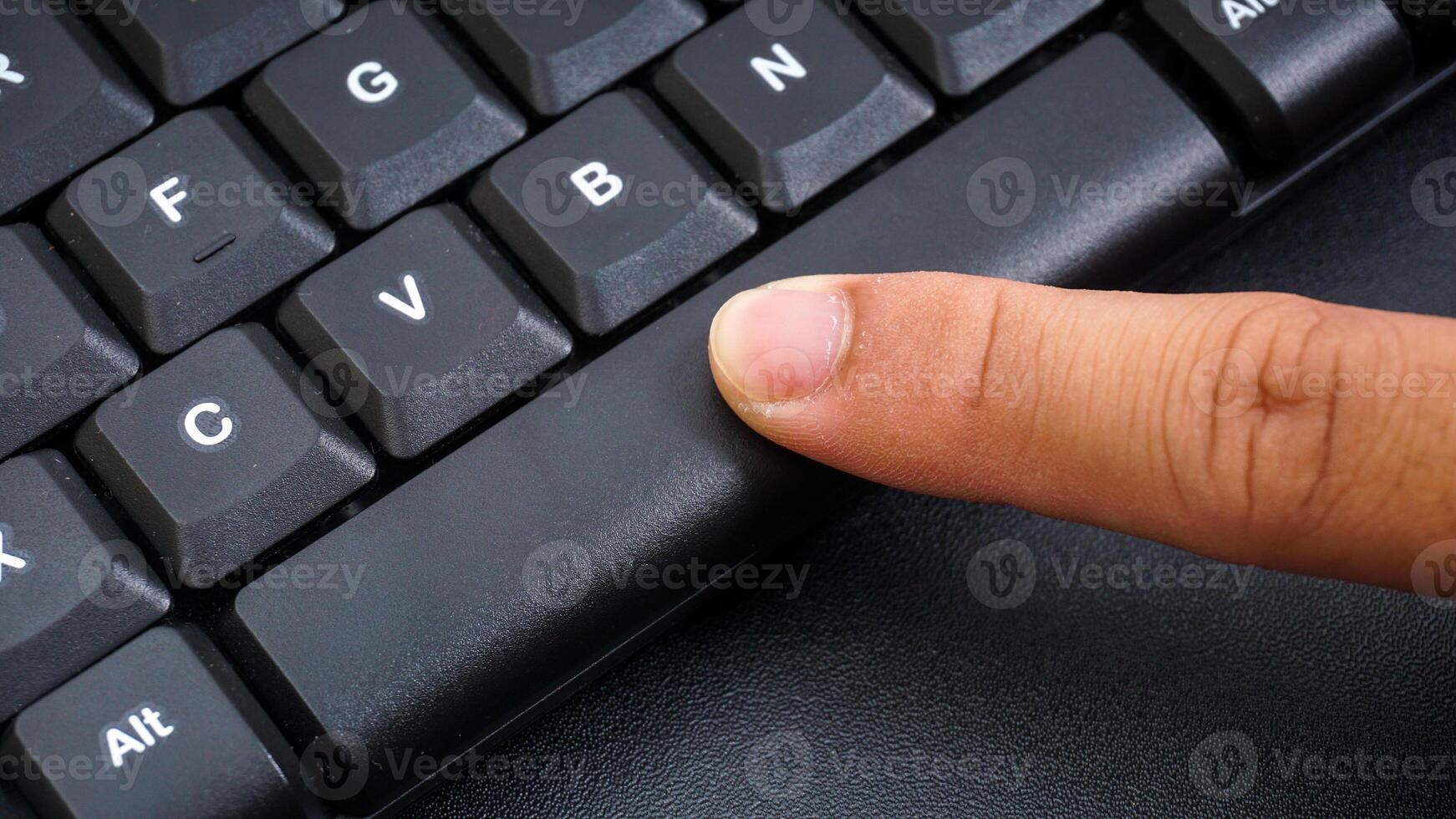 Close up on finger pressing space button on a computer keyboard isolated on black background photo