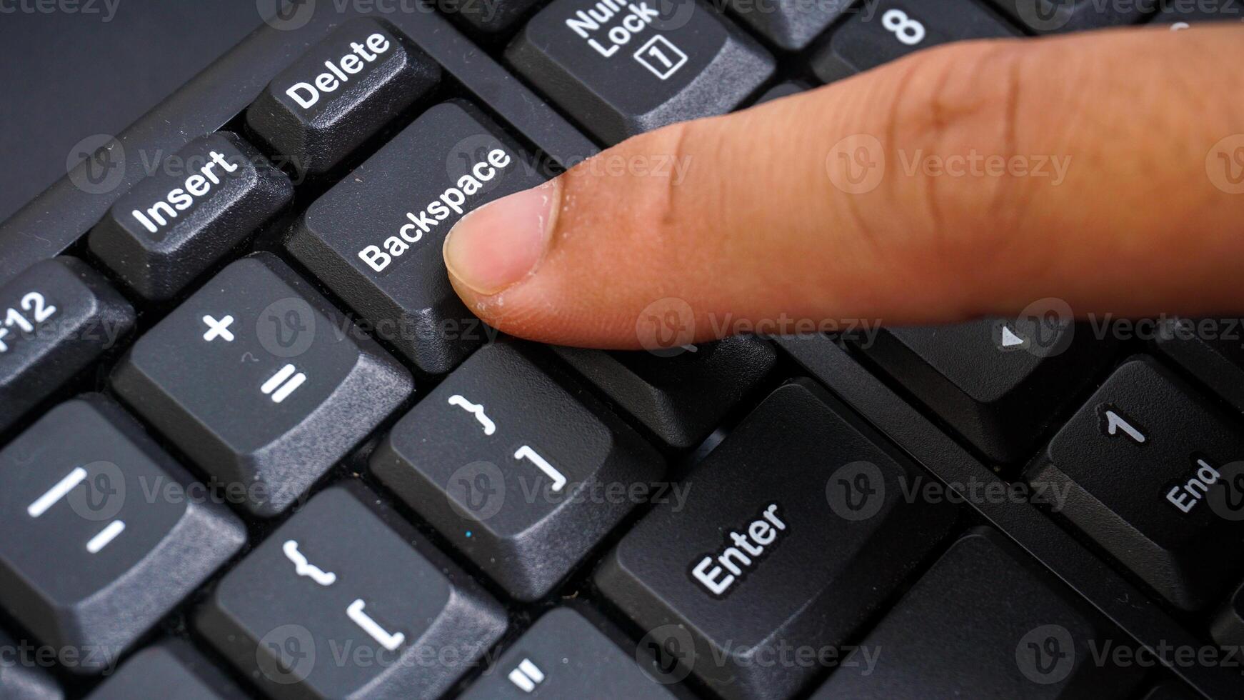 Close up on finger pressing backspace button on keyboard isolated on black background photo